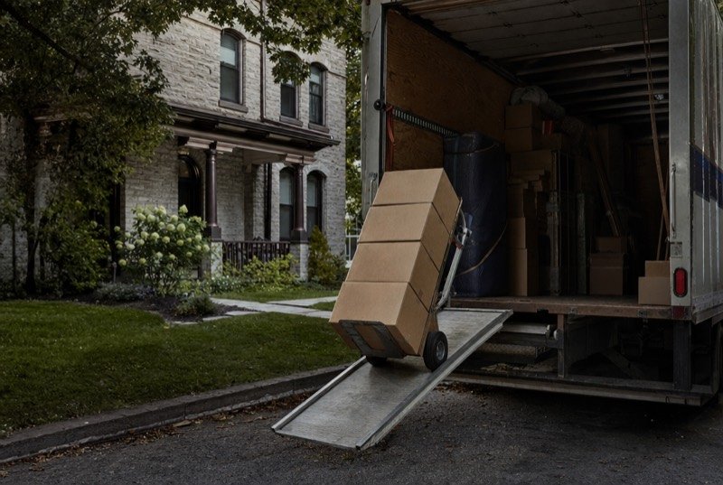 Cardboard moving boxes stacked on a hand dolly at the ramp of a moving truck in a driveway
