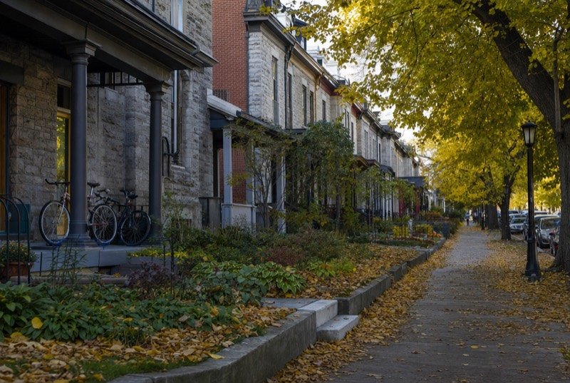 A row of old grey stone and red-brick semi-detached houses with bicycles on a porch and autumn leaves